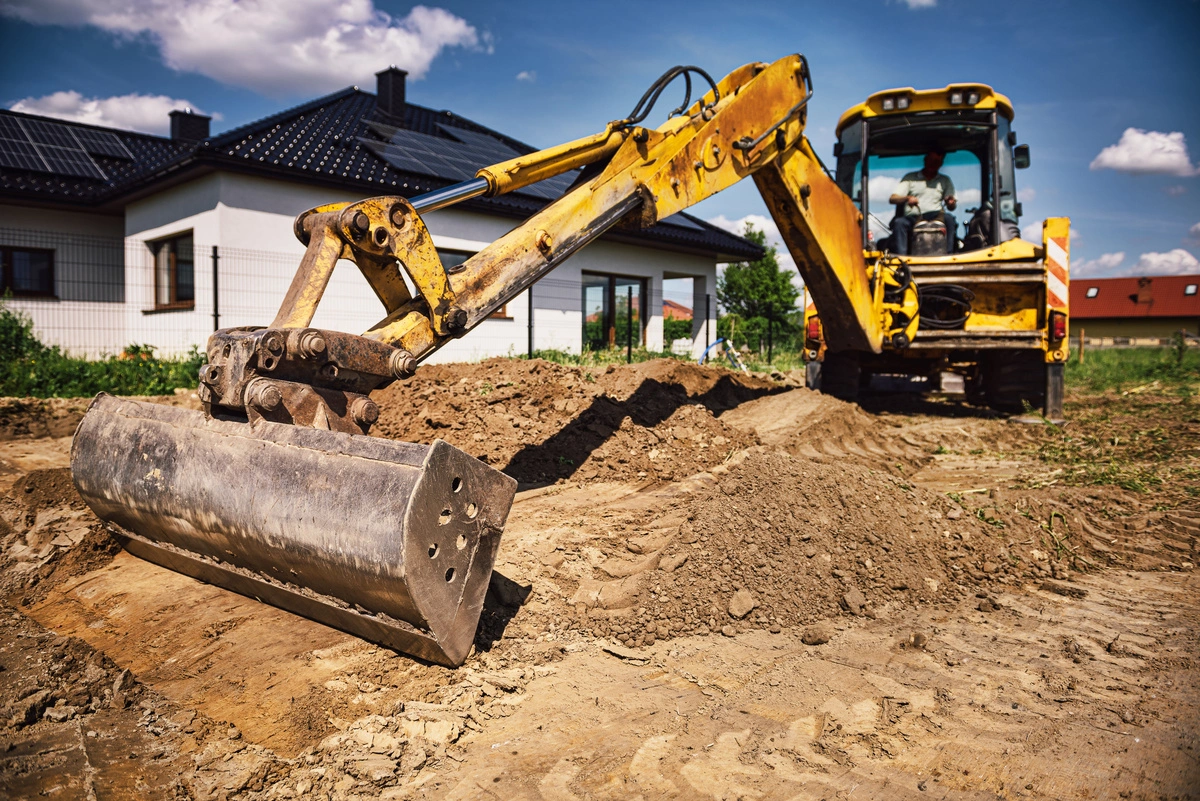 Engin de chantier effectuant un nivellement de terrain devant une maison, montrant l'importance du terrassement pour les projets de construction